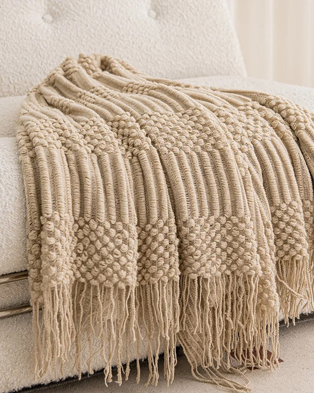 Oat knitted throw with tassels draped over a cream sofa
