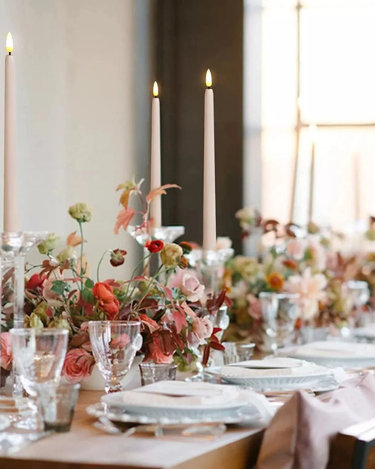 Flameless taper candles on a set dinner table with flowers