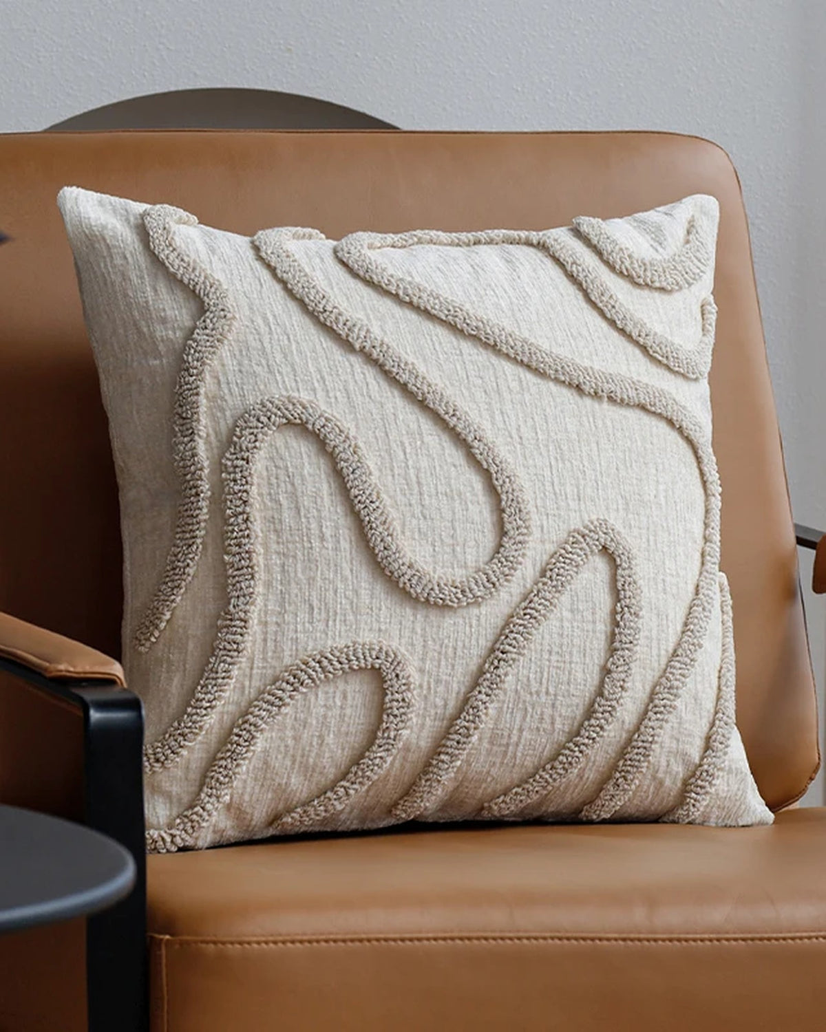 Cream tufted cushion cover with oat wavy lines on a tan leather armchair